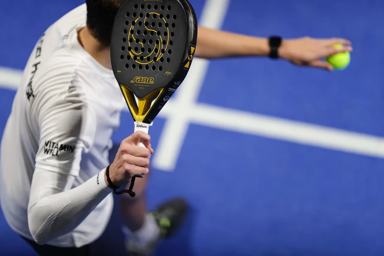 Joueur de padel au service, raquette noire et jaune et balle en l'air sur un court bleu
